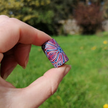 Hand holding a small, colorful object with a blurred green outdoor background