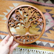 Wooden tree of life decorative item held against a patterned fabric background