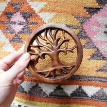 Wooden tree of life ornament held by a hand on a patterned rug