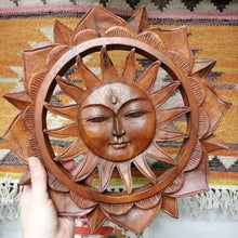 Wooden sun wall art with face held by a hand against a patterned fabric background