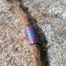 Multicolored striped bead on a piece of hair against a textured stone background