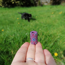 Hand holding a colorful cylindrical object with a blurred background of a grassy area and a cat.