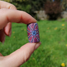 Hand holding a small, colorful dreadlock bead against a blurred green outdoor background