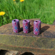 Three colorful cylindrical objects on a stone surface with grass and flowers in the background